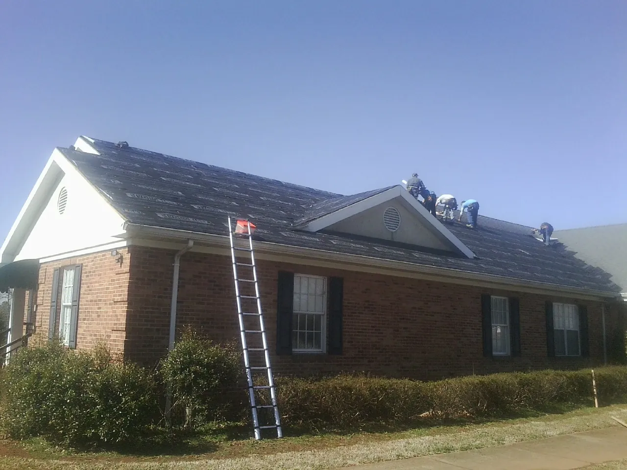 Crew tearing shingles off a brick ranch roof with a ladder set — Metal Roof Repair work by our crew in Union City